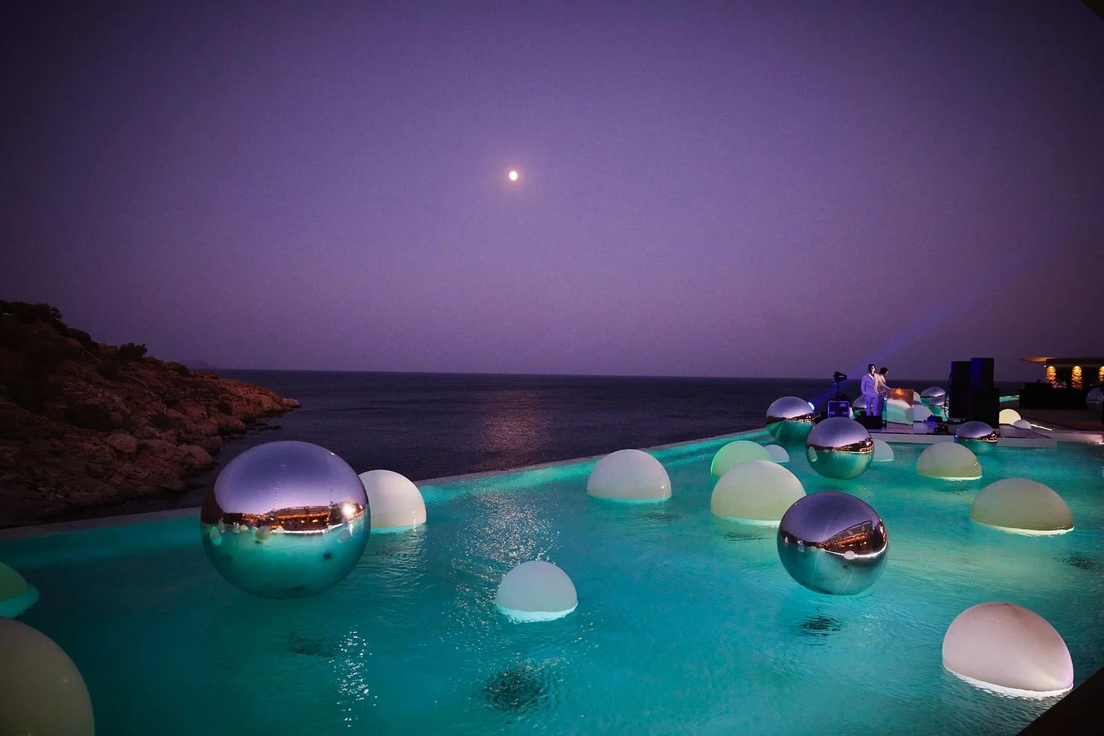Chrome balloon orbs reflecting moonlight over a pool at a private event in Mykonos