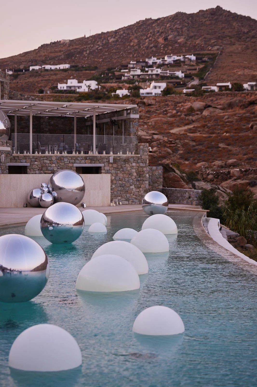 Chrome balloon orbs floating above an infinity pool at dusk